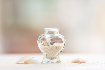 Bright composition with coral sand and sea shells in a glass bottle standing on a wooden table