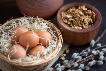 Vintage food composition with eggs in braided basket and nuts in wooden bowl