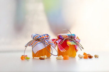 Two glass small pots of orange jam corded by string and cotton fabrics standing on a table