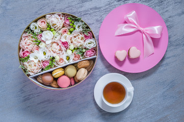 Gift boxes with fresh flowers, macarons  and cup of tea on blue background. Holiday card. Copy space, top view. Spring is coming...