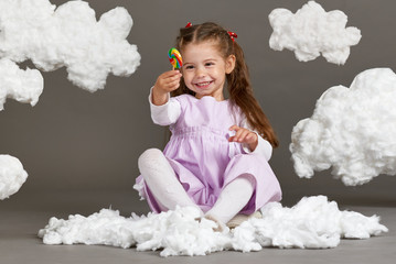 girl girl eating candy and playing with clouds, shooting in the studio on a gray background, happy childhood concept