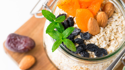 Healthy breakfast in glass mason jar with oat flakes, granola, milk, dry fruits and nuts, dates, honey, orange juice, eggs for morning fitness on wooden board platter on white background isolated