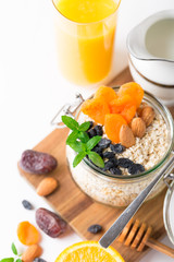 Healthy breakfast in glass mason jar with oat flakes, granola, milk, dry fruits and nuts, dates, honey, orange juice, eggs for morning fitness on wooden board platter on white background isolated