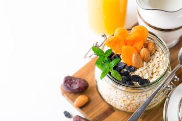 Healthy breakfast in glass mason jar with oat flakes, granola, milk, dry fruits and nuts, dates, honey, orange juice, eggs for morning fitness on wooden board platter on white background isolated
