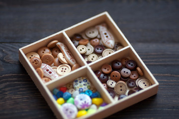 Different colorful decorative clothes buttons in a wooden box
