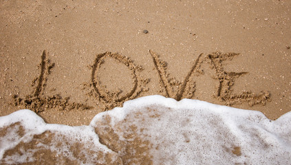 LOVE inscription on the beach sand and sea wave.