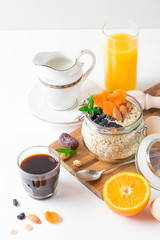 Healthy breakfast in glass mason jar with oat flakes, granola, milk, dry fruits and nuts, dates, honey, orange juice, eggs for morning fitness on wooden board platter on white background isolated