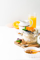 Healthy breakfast in glass mason jar with oat flakes, granola, milk, dry fruits and nuts, dates, honey, orange juice, eggs for morning fitness on wooden board platter on white background isolated