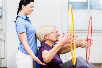 Physio instructing senior man and woman during gymnastic exercise
