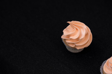 One capcake on a black background with orange cream. View from above.