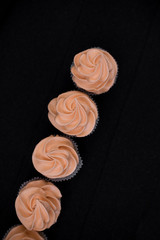Close-up five cupcakes on a black background with orange cream. View from above. In one line diagonally.
