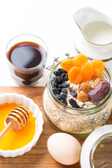 Healthy breakfast in glass mason jar with oat flakes, granola, milk, dry fruits and nuts, dates, honey, orange juice, eggs for morning fitness on wooden board platter on white background isolated