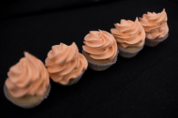 Close-up five cupcakes on a black background with orange cream. View from above. In one line diagonally.
