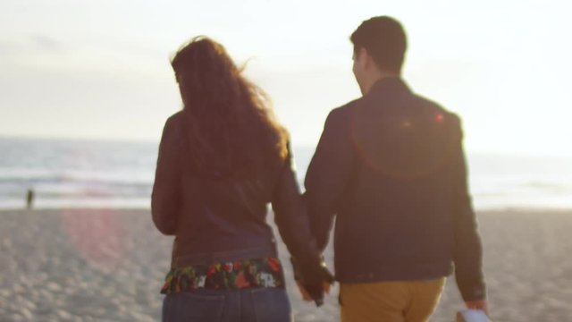Happy Couple Hold Hands And Enjoy Walking On The Beach At Sunset (Slow Motion)