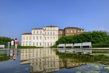 Venaria reale, Piedmont region, Italy. June 2017. The facade of the palace, on the side of the gardens, is reflected on the fountain's water mirror. Tourists explore the magnificent park.