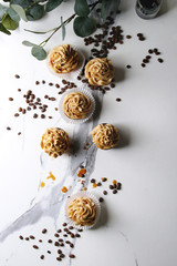 Fototapeta na wymiar Fresh baked homemade cupcakes with coffee buttercream and caramel with eucalyptus branch and coffee beans above over white marble background. Flat lay, space