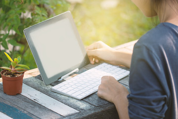 Woman is using a tablet and typing keyboard in the garden.