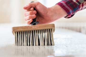 Close-up of the hand of a man holding a synthetic brush with plastic handle while applying paste to...