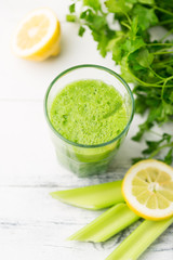 Green cocktail smoothie parsley celery lemon lime slices, healthy drink ingredients, glass of beverage on white wooden table, detox diet clean eating, with vegetables on table