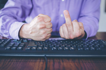 Agression in the Internet, man sitting behind keyboard with hand clenched into a fist and middle...