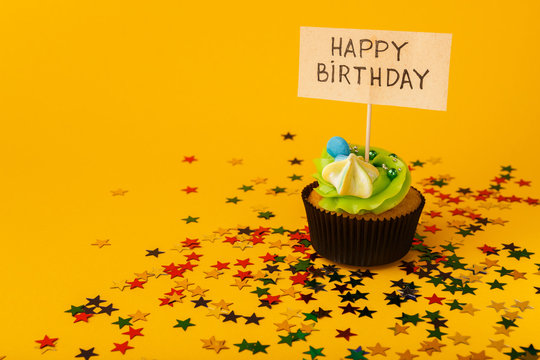 Birthday cupcake with greeting card on yellow background