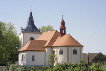 Church named Nanebevzeti panny Marie in Vraclav village, sacral historic heritage with tower nad red roof on the hill, blue sky