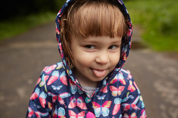 Funny little girl in rain coat stands in green park