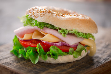 Sesame bagel sandwich with lettuce, tomato, yellow cheese and ham.