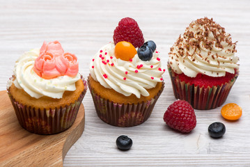 Cupcakes with white cream decorated with strawberry,  blueberry and chocolate chips on wooden background