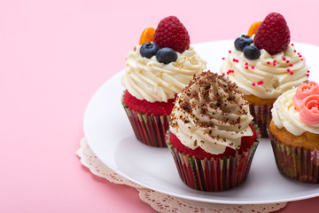 Cupcakes with white cream decorated with strawberry,  blueberry and chocolate chips on pink background