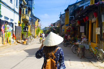 Woman tourist is wearing Vietnamese Hat (Non La) and traveling in Hoi An old town in Vietnam.
