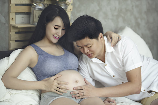 Young Pregnant Asian Woman Holds Her Hands on Her Swollen Belly, Love Concept.