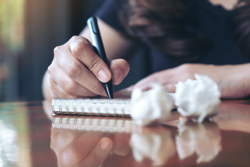 Closeup image of a businesswoman working and writing down on a white blank notebook with screwed up papers on table © Farknot Architect