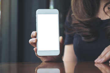 Mockup image of a woman holding and showing white mobile phone with blank screen in cafe