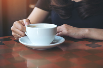 Closeup image of a woman holding and drinking hot coffee in cafe