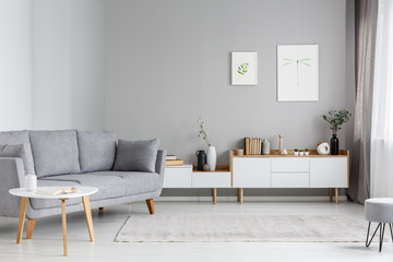Grey settee near white cupboard in minimal living room interior with posters on the wall. Real photo - 207008810