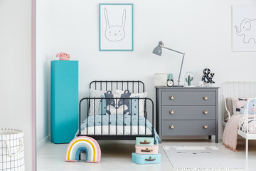 Lamp on grey cabinet next to black bed and blue pedestal in siblings bedroom interior. Real photo