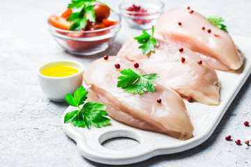 raw chicken breasts on cutting board with herbs,oil,tomatoes. Selective focus, copy space.