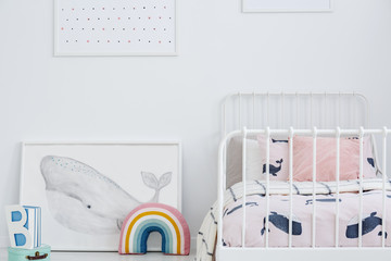 Whale poster and rainbow next to white bed in bright kid's bedroom interior. Real photo
