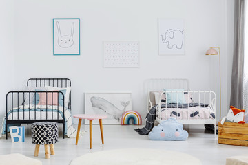 Patterned stool in spacious children bedroom interior with posters above white and black bed. Real photo
