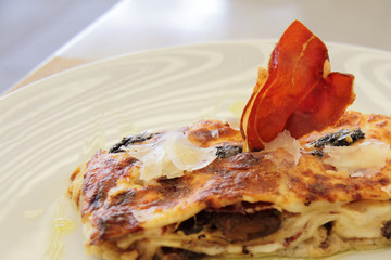 piece of lasagna on white plate with slice of jamon 