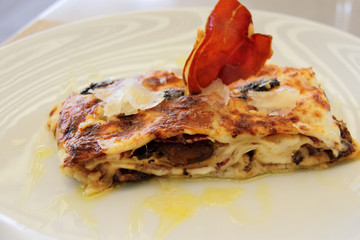 piece of lasagna on white plate with slice of jamon 