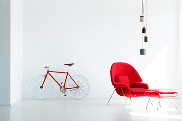 Red bicycle and armchair under lamp in white minimal apartment interior. Real photo