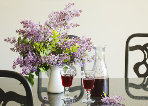 Berry drink in glass and bouquet of lilac in the table