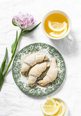 Cup of green tea with lemon, mini croissants, tulip flower - morning cozy still life on a white background, top view.Flat lay