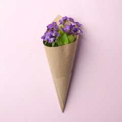 violet flowers in cone on pink background, flat lay. Spring, summer romantic minimal concept