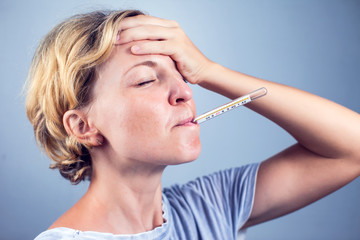 Sick woman with seasonal flu measuring body temperature with thermometer in her mouth reaching 38...