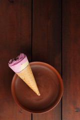 Ice cream cone with chocolate. Ice cream in a waffle cup on a dark wooden background. Cold milk dessert on a clay plate. Copy space. Summer cold dessert