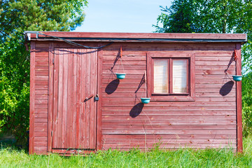 Деревянная постройка стоит на лугу, на фоне зеленых деревьев и неба © Fotograf