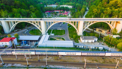 Fototapeta premium Drone view of the Matsesta viaduct and railroad with train on the background of the dense forest in summer day, Sochi, Russia 